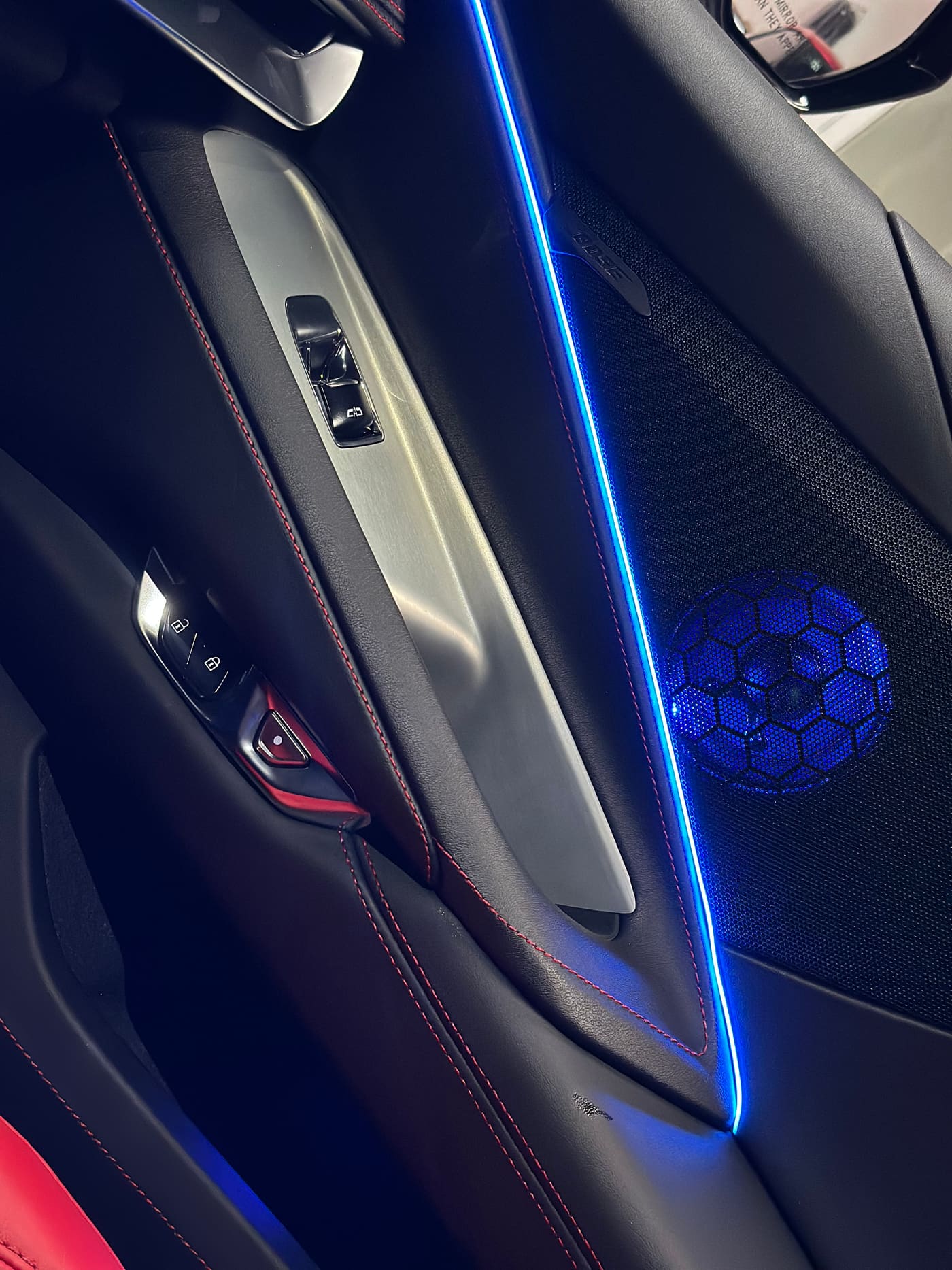 Blue ambient lighting tracing the door panel and glowing speaker grille in a Corvette